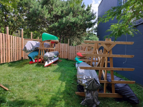 Kayaks, canoes and paddleboards on wooden storage racks inside the fenced area