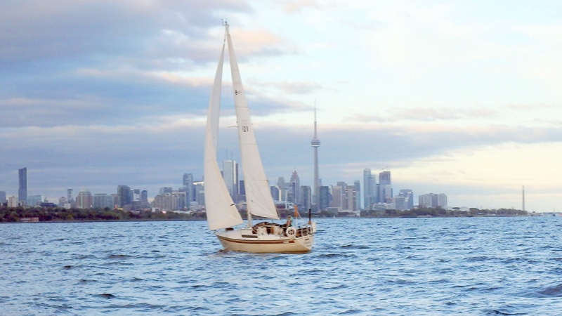 A sailboat on Lake Ontario with the Toronto skyline and CN Tower behind