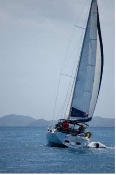 A sailboat with a crew aboard, sailing past hills on the horizon