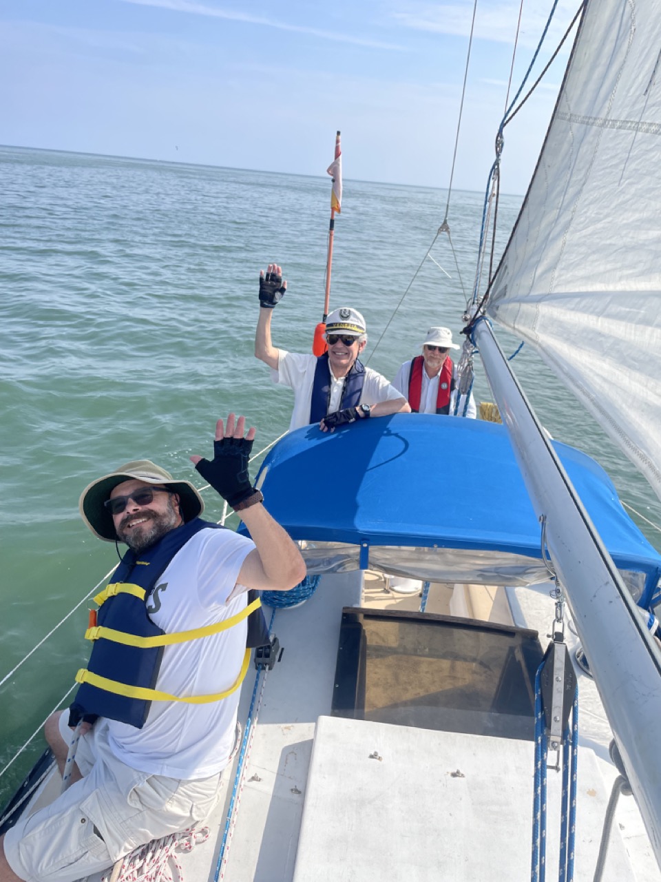 Three smiling sailors in life jackets waving from the deck of a sailboat